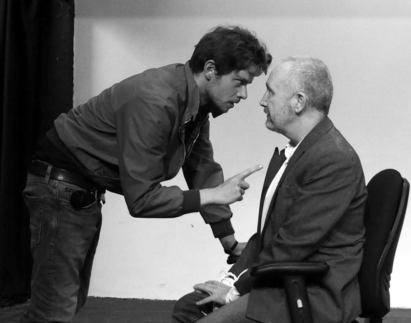 A man points at another man tied up in a chair