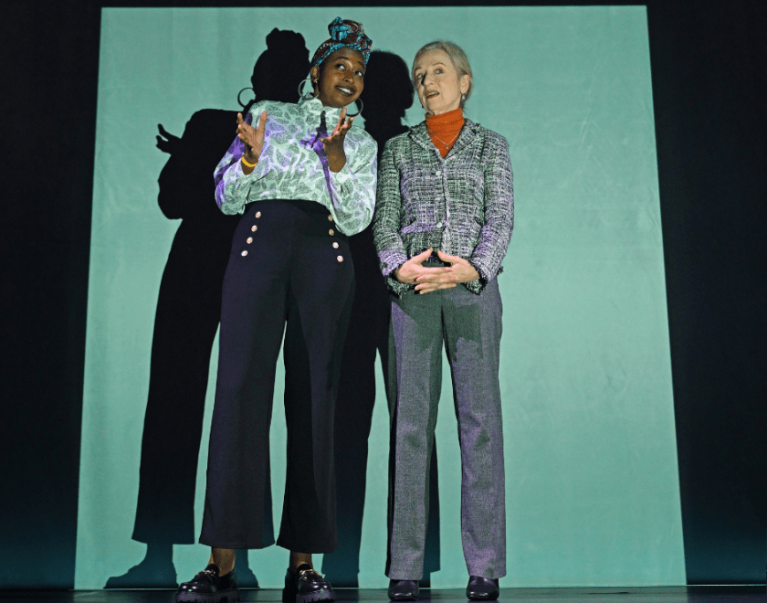 Production photo: Two women stand side by side illuminated by a square of projected light.
