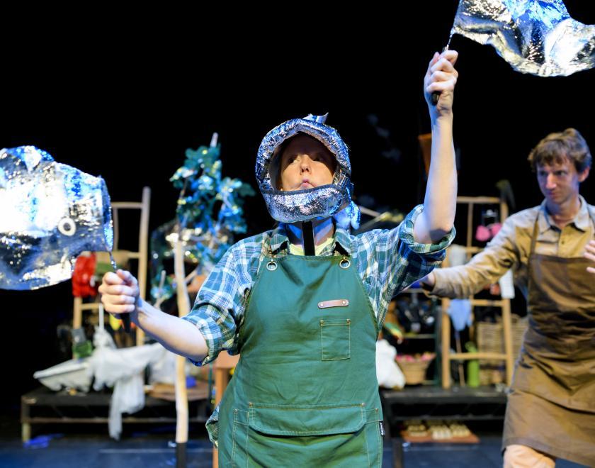 A different photo of the performer with a fish hat on, holding two fish puppets.