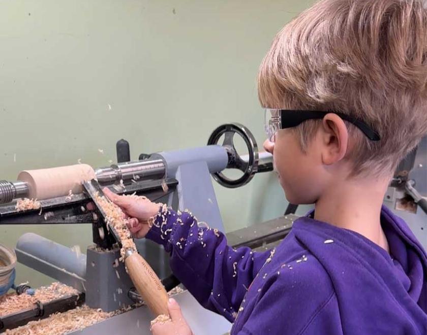 A boy turning at the lathe using the roughing gouge.