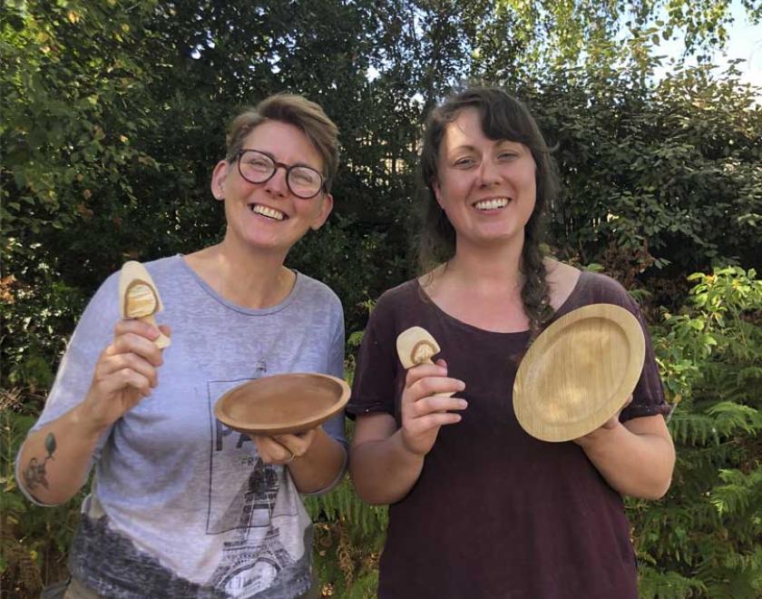 A pair of smiling women holding their completed wooden mushrooms and bowls.