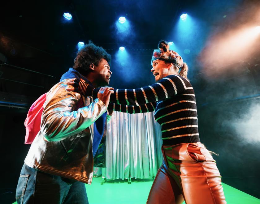 Photo of two cast members performing a scene, clinging on to each other as if in a desperate situation.
