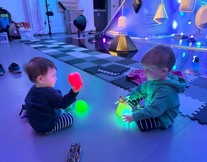 Photo of two babies playing with coloured lights in front of the set for 'Kaleidoscope'
