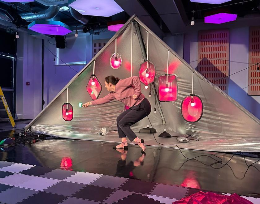 Photo of a performer striking a pose while holding a coloured light during a 'Kaleidoscope' performance. 