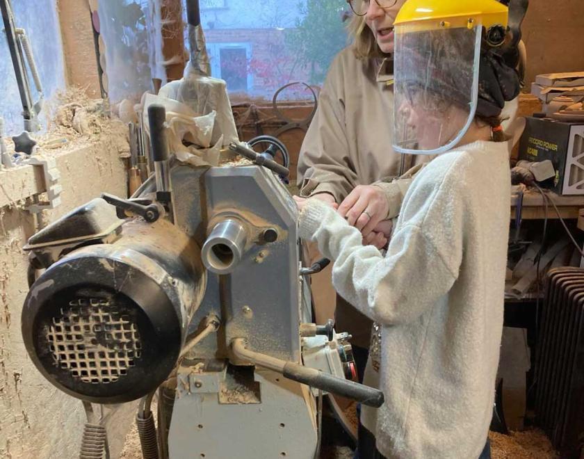 A girl wearing a face visor and working at a lathe