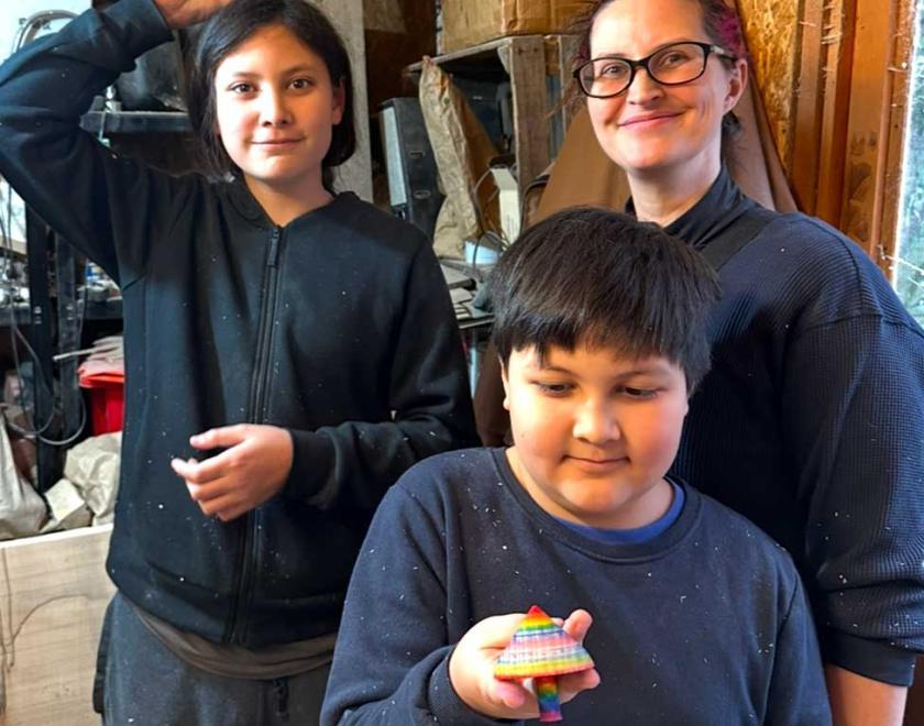 A smiling mother with two sons each holding a colourful wooden spinning top