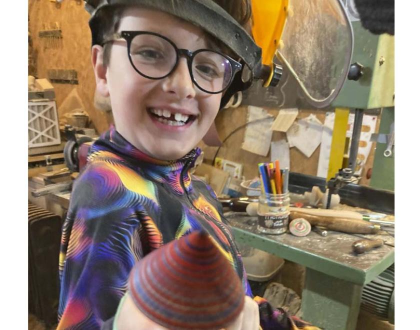 A boy holding his own wooden spinning top.