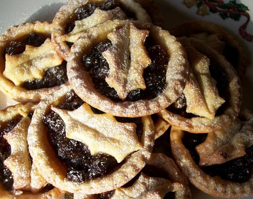 Photo of a pile of mince pies. The mince pies are topped with pastry shapes of holly leaves