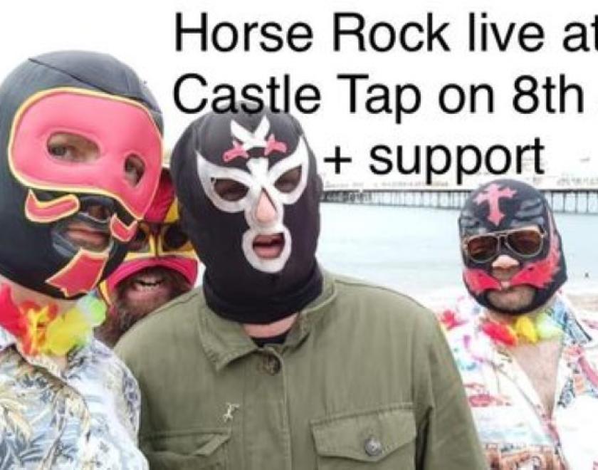 Three people in luchador masks are standing on the seaside looking at the camera