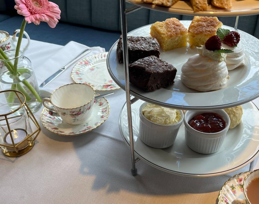 Metal table stand with various sandwiches and cakes, a vintage tea cup and a vase with a pink flower