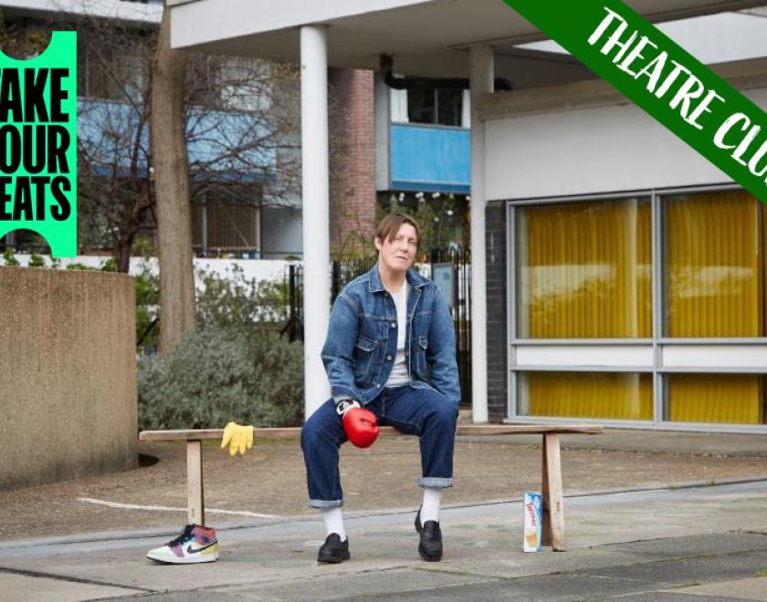 Photograph of Tink Flaherety sitting on a bench outside some office buildings. White text reading 'Theatre Club' is overlaid across the top right corner and the 'Take Your Seats' logo is in the top left corner