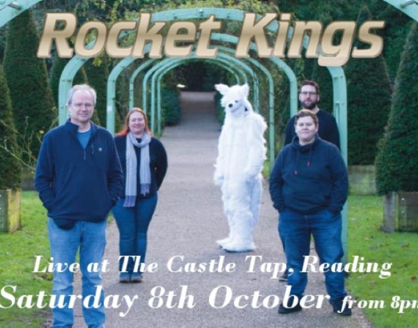 Five figures stand on a path facing the camera. The path stretches straight back into the distance in the centre of the image; it has a series of teal arches over it and sculpted evergreen trees on grass either side. Three of the figures are wearing blue jeans and navy blue comfy jumpers, the head of a fourth figure is visible almost directly behind one of the front individuals and finally at the back of the group a fifth figure is dressed head-to-toe in a white furry animal suit