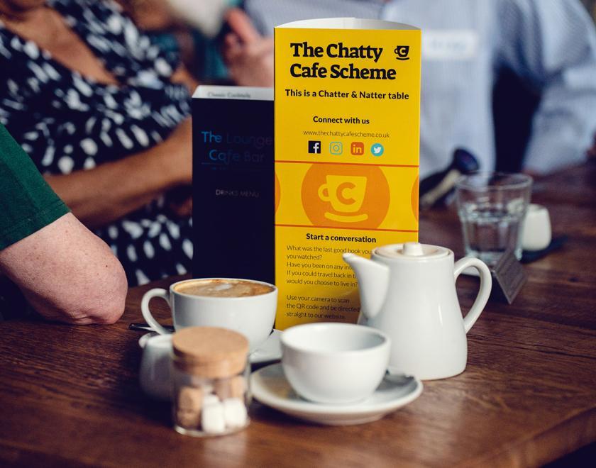 Image of a Chatty Cafe table flyer on a table with coffees