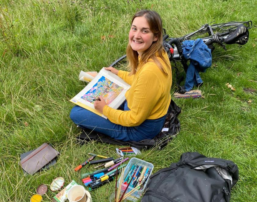 Christabel Forbes sat down on grass captured mid drawing 