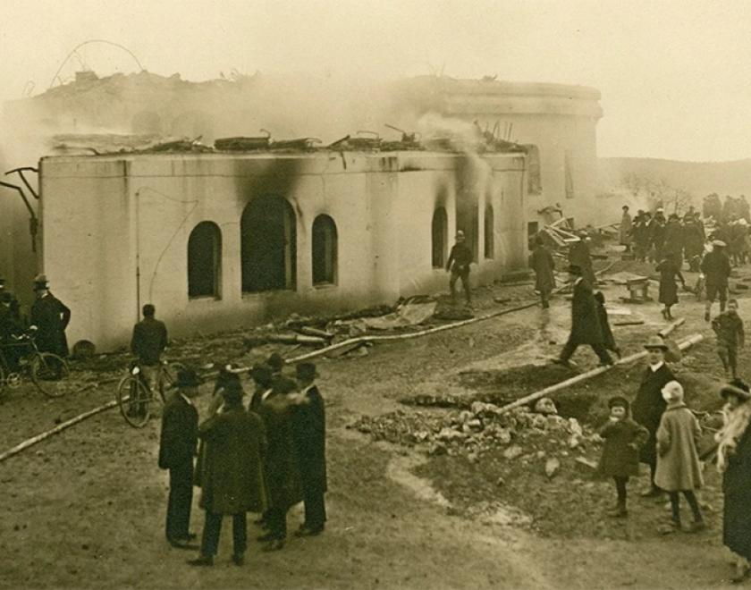 Sepia image of a burnt building with a small group of people stood in the foreground.