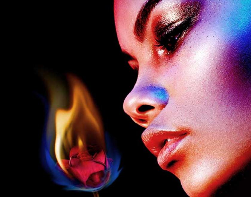 A woman with neon glittered makeup looking at a flower covered in a dull flame 