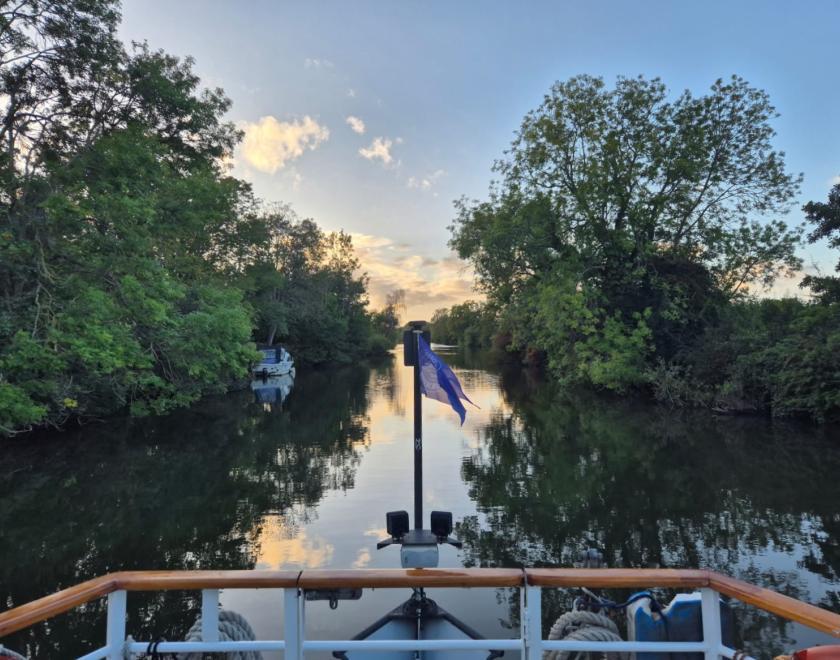 front of the boat with thames rivercruise flag river scene with foliage on either side of the bank