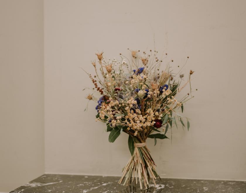 Beautiful bouquet of dried flowers standing up on black marble mantlepiece against white wall.