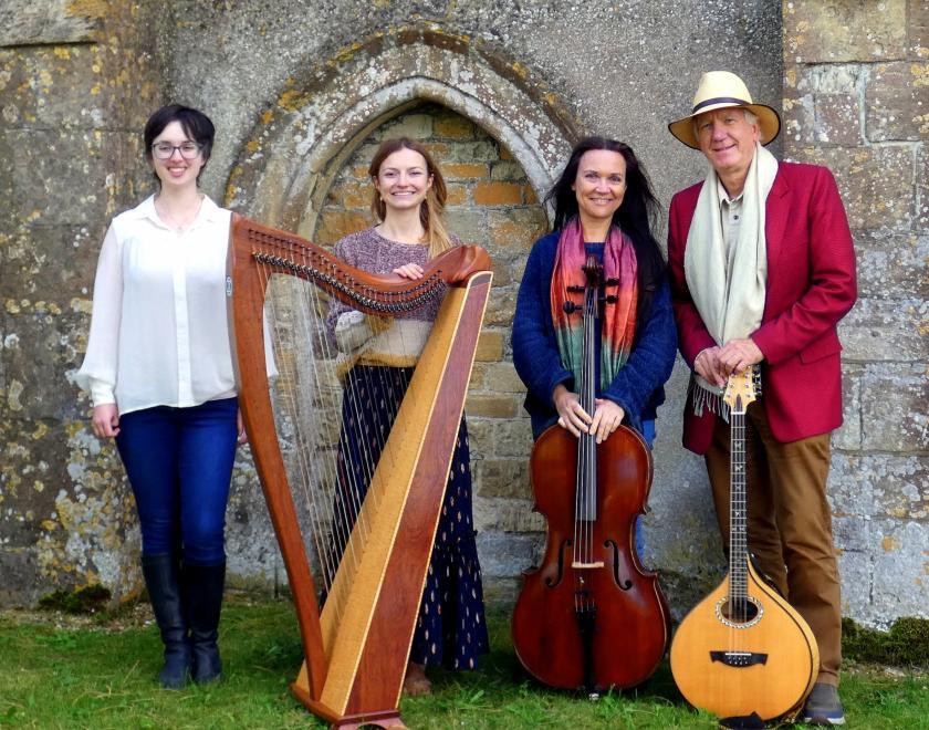 Photo of the four members of Moonrakers with musical instruments. They are standing in front of an old building with an arched doorway, like a church.