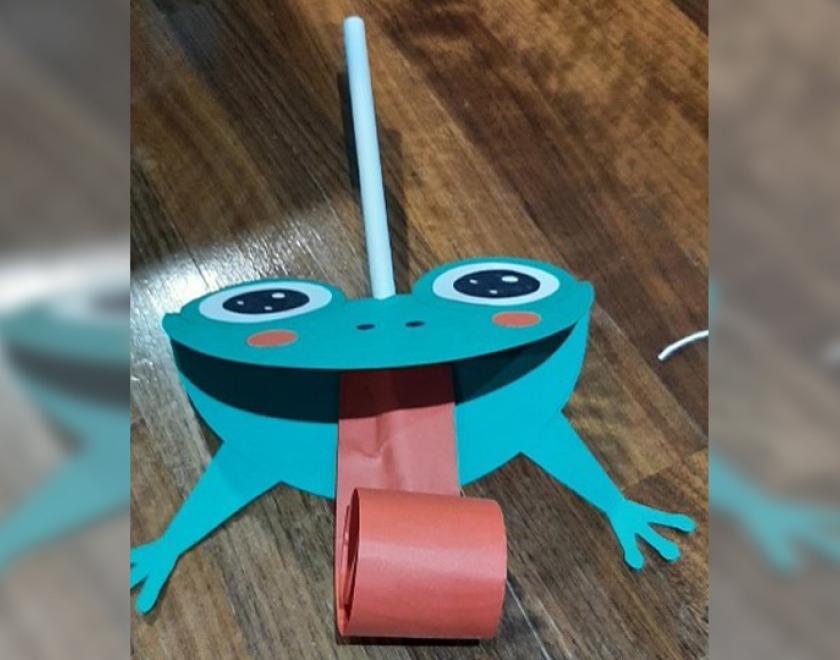 Photograph of a cardboard green frog sticking out a long pink tongue