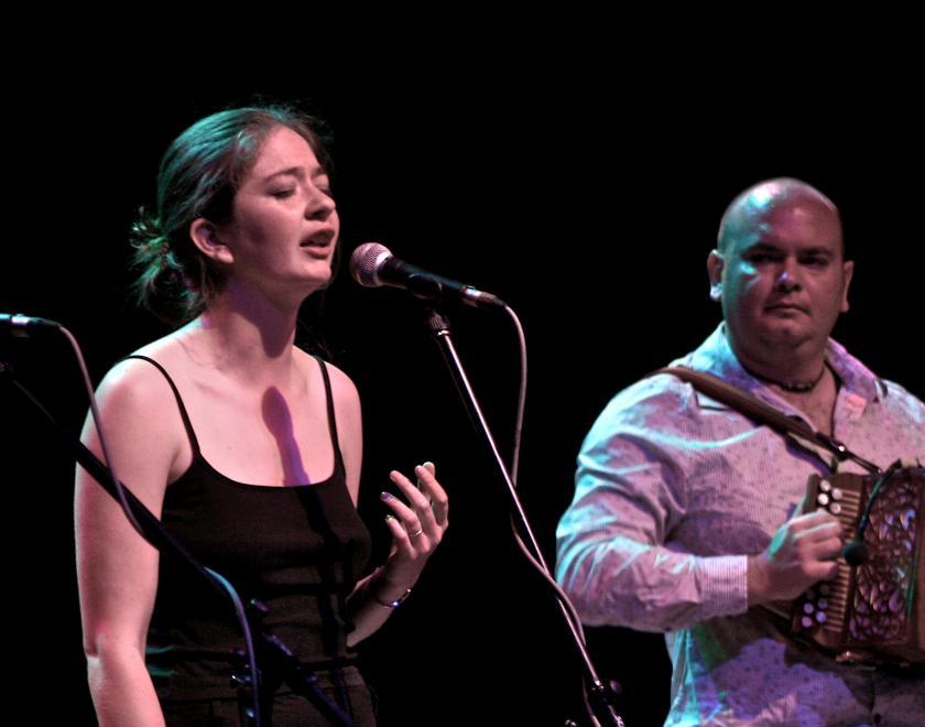 Photo of Jess and Rich Arrowsmith on stage. Jess is singing and Rich is playing a melodeon.