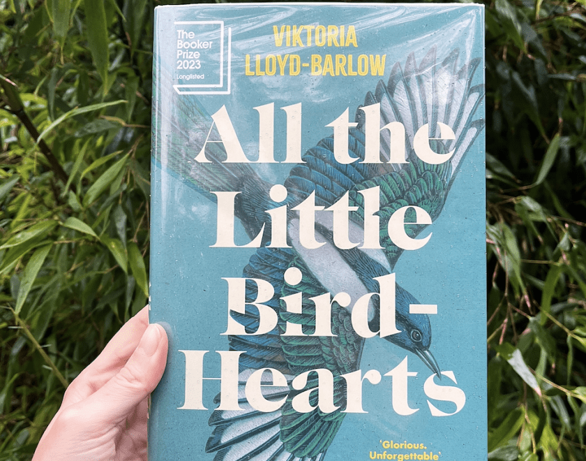 book titled all the little bird hearts held up in front of green plants