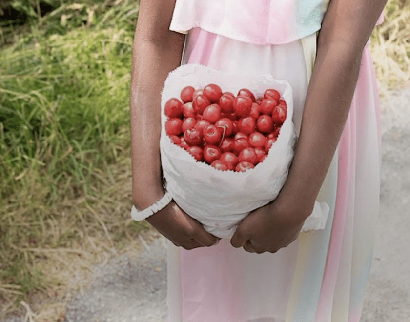 arms holding a bag of cherries with views of a garden behind