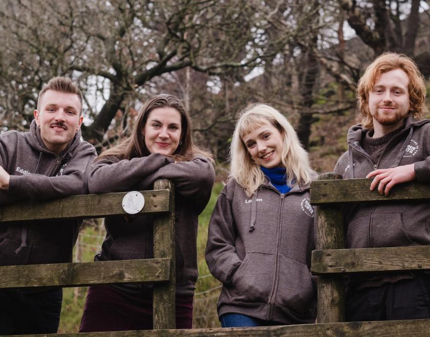 four actors stood behind a fence in the countryside