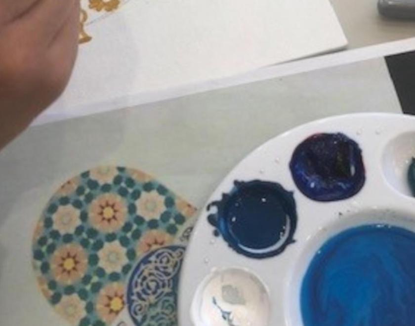 close up of a hand painting, next to a paint palette