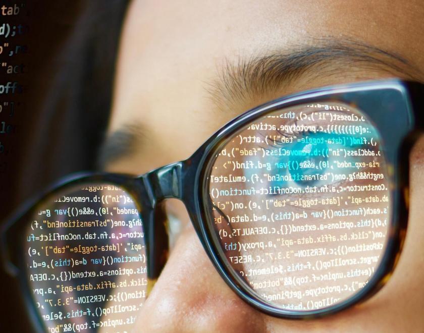 close-up of a girl wearing glasses with computer code reflected in them