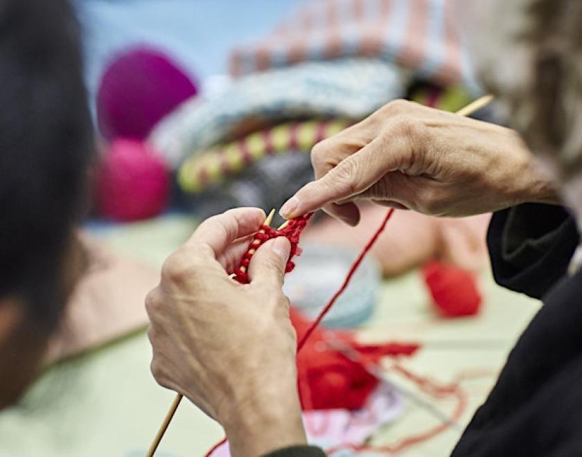 A close up of hands knitting with red yarn