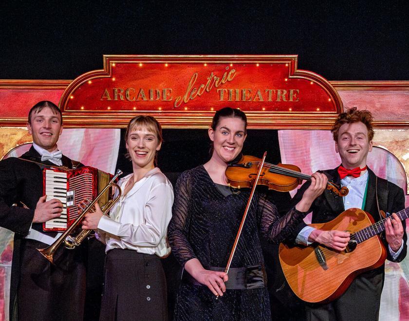 four actor-musicians in smart dress holding musical instruments in front of a painted backdrop