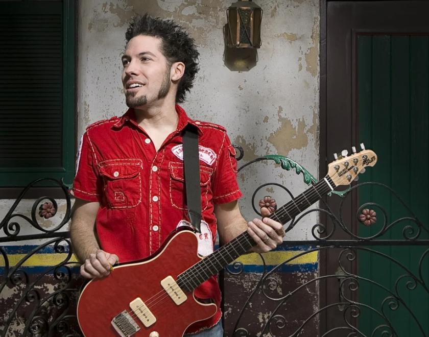 A man in a red shirt, holding a red guitar