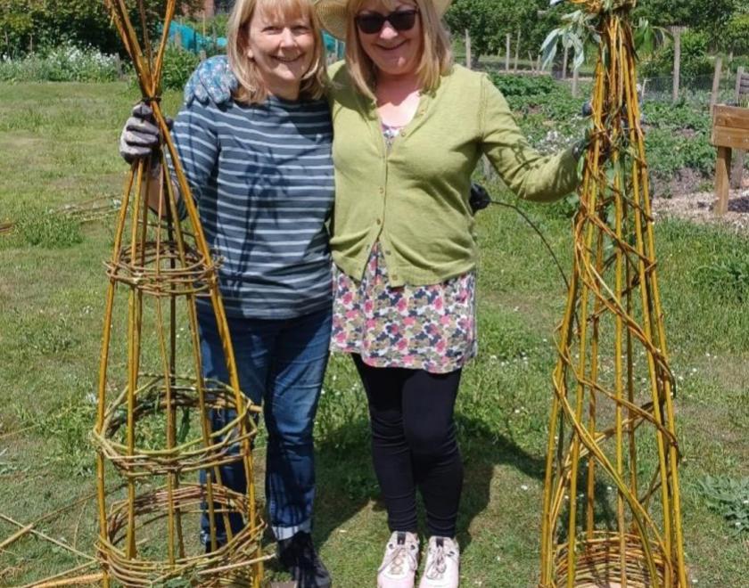 Two women in gardning clothes, each holding a willow obelisk