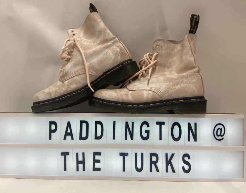 A pair of white Doc Martens over a sign saying "Paddington @ the Turks"