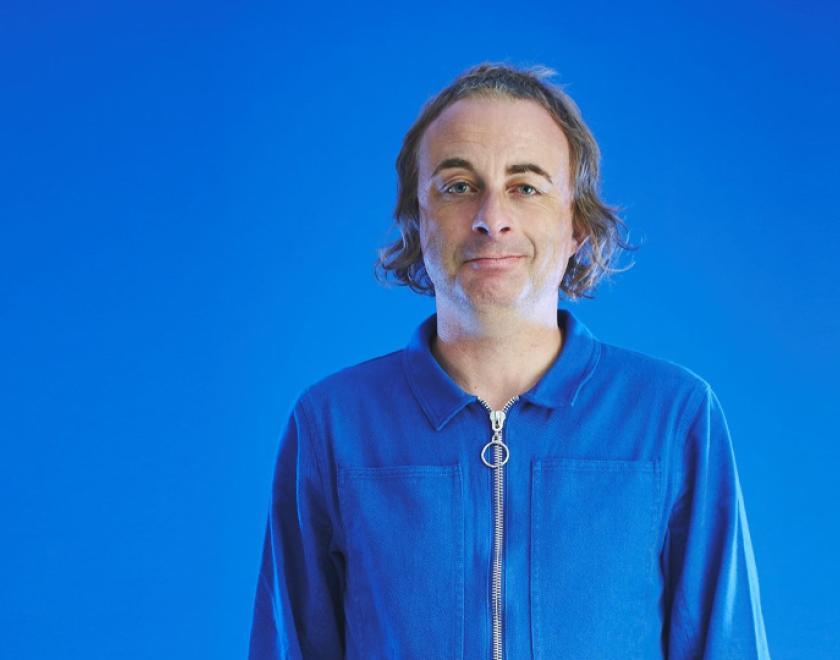 Comedian Paul Foot in a blue jumpsuit against a blue background