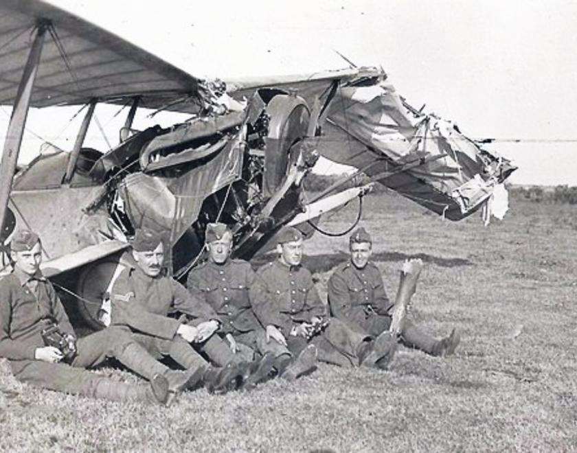 photo of five men sitting in front of a crashed plane