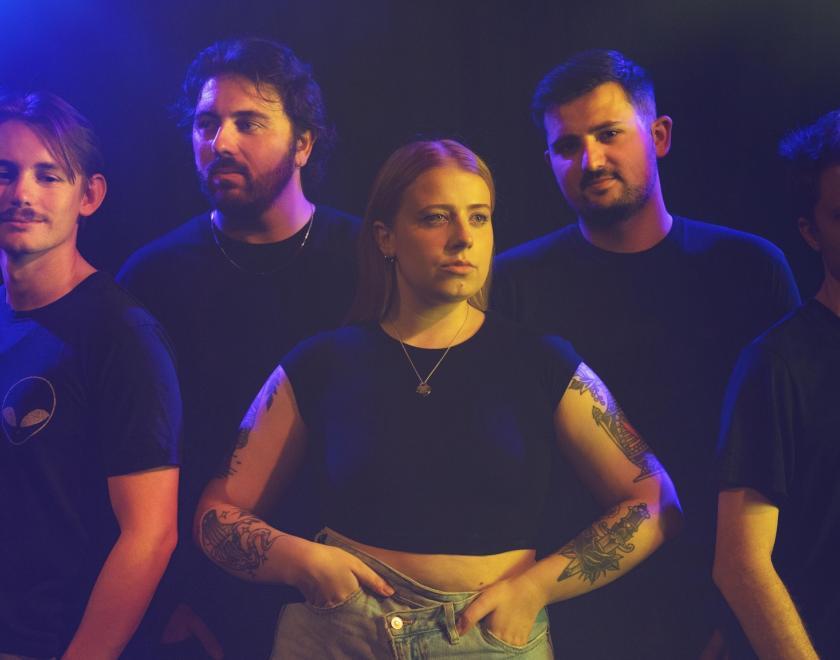 Five band members standing under purple lights