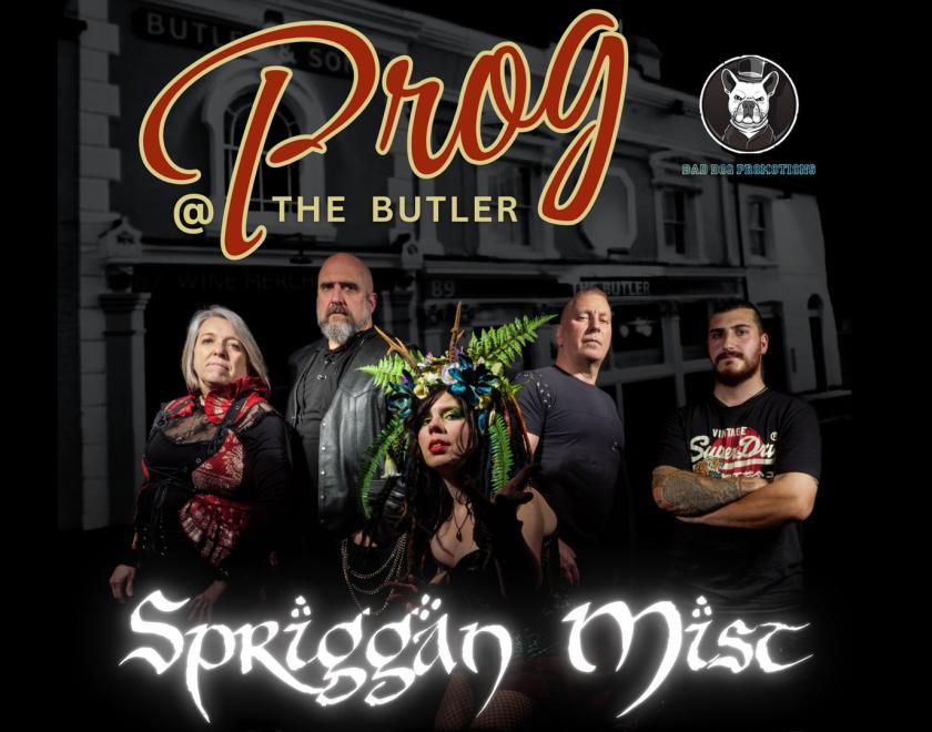 Prog band Spriggan Mist standing in front of a picture of the Butler Pub. Two women and three men, they are variously dressed in "alternative" clothes - lots of leather, fishnets, horned headpieces and the like