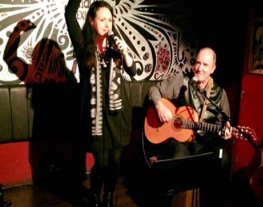 Photo of Skinner and T'witch on stage. In the photo Sandra Twitchett is singing, with her arm raised above her head and Steve Skinner is playing guitar.