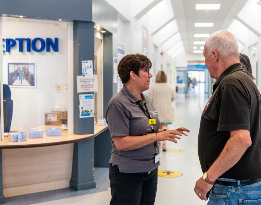 A volunteer speaking to a visitor in a hospital reception area