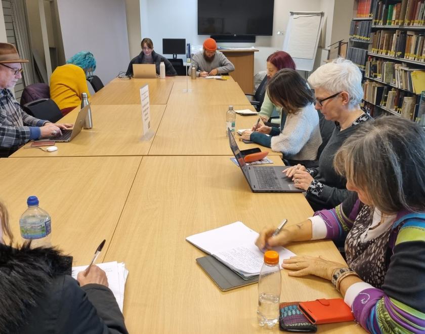 various people sitting around a big table in a library. All are writing.