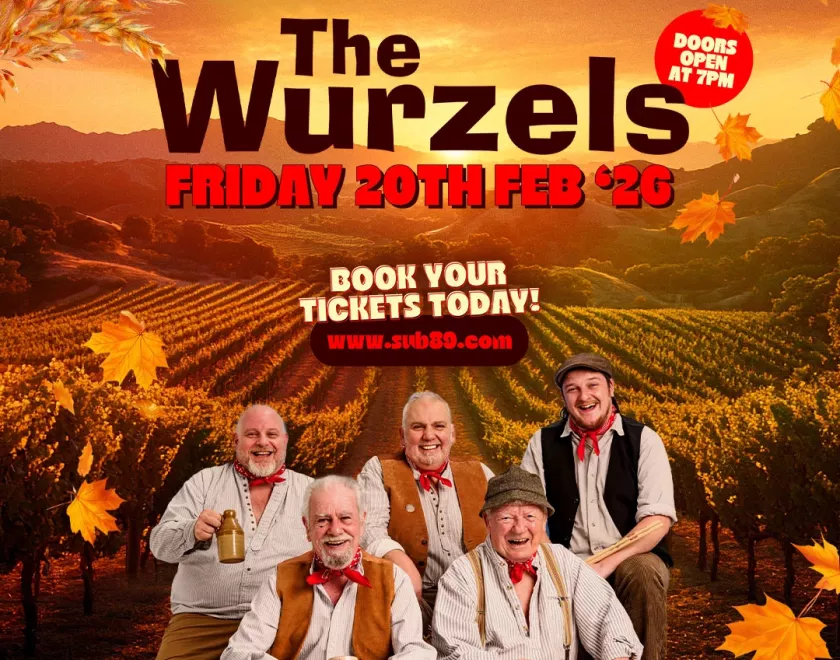 The Wurzels wearing country clothes and standing by a fence